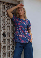 Woman poses in short sleeved  blue floral cotton top with empire waistline and deep pockets, paired with sea blue cotton pants