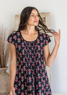 Close up of a woman poses in a 100% cotton navy black based floral dress with round neckline and cap sleeves