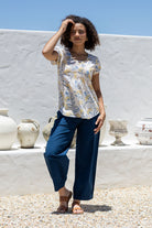 Woman wears neutral based floral print 100% cotton cap sleeve top with pin tuck detail across the bust and a scoop neckline