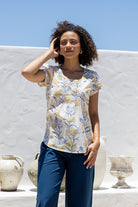 Woman wearing a neutral based floral print short sleeve top with scoop round neckline and pleated detail across the bodice