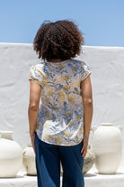 Woman standing backwards wears 100 percent cotton top with short cap sleeves and longer back hem.