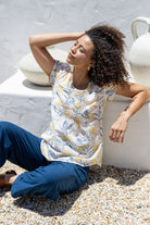 Woman sitting outdoors wearing 100% cotton floral top and blue pants.