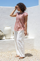Woman standing sideways wears 100 percent cotton top with short cap sleeves and longer back hem.
