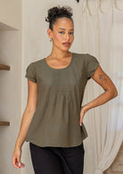 Woman wearing a green cotton short sleeve top with a scoop neckline and pin-tucks across the centre bodice paired with black pants