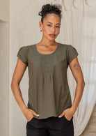 Woman wearing an olive green top and black pants standing with hands in pockets