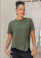 Woman wearing an olive green twist-front rayon T-shirt with short sleeves and a subtle draped knot at the front over black cotton pants