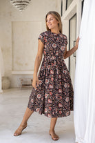 Woman poses in 1950's style short sleeved, button through cotton dress with high round neckline in dark based indian floral print.