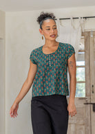 Woman wearing a green based floral print 100% cotton top with coconut buttons.
