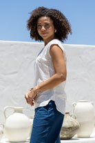 Woman in a white sleeveless cotton top that is longer at the back, paired with blue pants