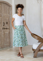 Woman is posing with one hand in pocket wearing a 100% cotton sage green a-line skirt.