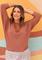 Woman wearing a 3/4 sleeve rayon batwing round neckline dusty pink top in front of colourful wall.