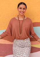 Woman with dark hair wearing a 3/4 sleeve rayon batwing round neckline dusty pink top with a floral skirt.