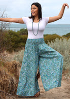 Model posing in aqua blue floral printed, 100% rayon pants with elastic waist.