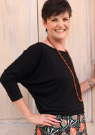 Woman with short dark hair wearing a 3/4 sleeve rayon batwing round neckline black top.