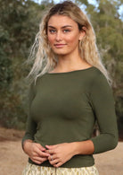 Woman with blonde wavy hair wearing a rayon boat neck olive green 3/4 sleeve top.
