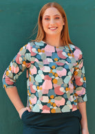 Woman wears spotty print cotton top in pinks, greens and blues on a teal base