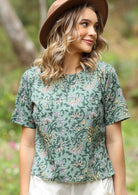Model wears cotton short sleeve relaxed fit top in floral print on a sage green base.