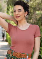 Woman wearing a scoop neck dusty pink rayon fitted t-shirt with tan belt and floral bottoms.