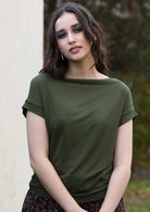 Woman with dark hair wearing a wide neck mod olive green stretch rayon boat neck top.