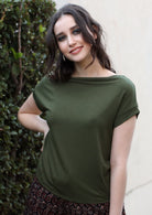 Woman wearing a wide neck mod olive green stretch rayon boat neck top with hand on hip.