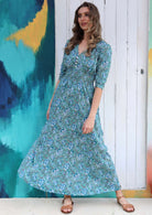 Model wearing a floaty rayon maxi dress in blue and white floral print on aqua blue base.